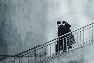 身穿黑夹克、戴黑帽子的男子站在灰色水泥楼梯上